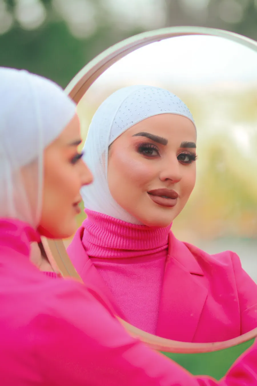 بورتريه لسيدة بحجاب أبيض وبدلة وردية ينعكس وجهها داخل مرآة دائرية في جلسة تصوير خارجية